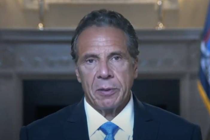 Governor Cuomo, in a suit and blue tie, talks to the camera